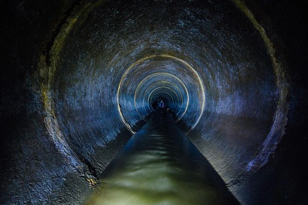 Dark underground sewer round concrete tunnel. Industrial wastewater and urban sewage flowing throw sewer pipe.